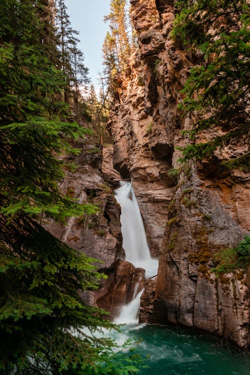 無料 茶色と緑色の岩層の間の滝 写真素材