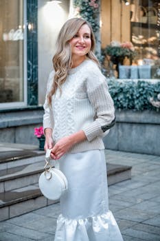 Side view attractive cheerful female in stylish elegant white outfit standing on street and looking away with toothy smile