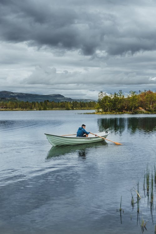 Free Anonymous man floating on canoe under cloudy sky Stock Photo