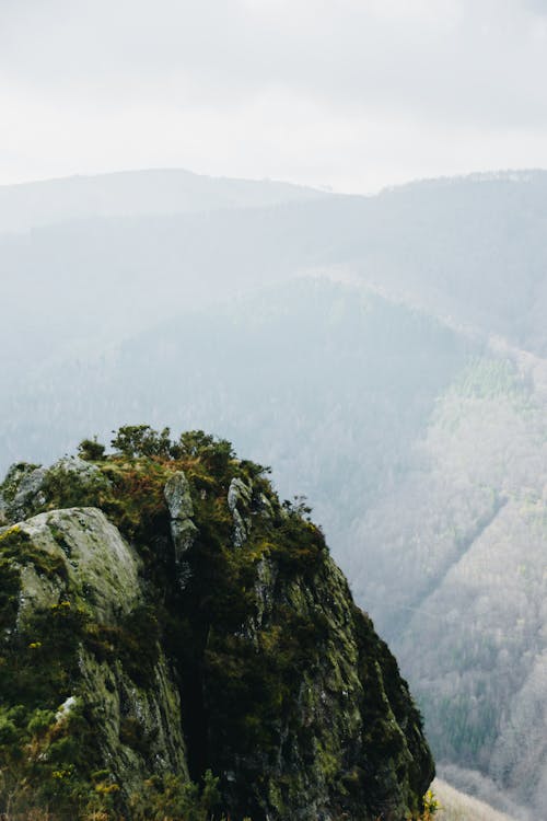 Picturesque view of rough rocky mountains with green vegetation against hills in cloudy weather