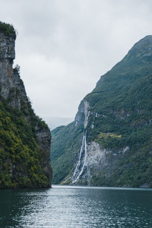 Free Magnificent landscape of wide river with rippling water surface flowing near massive rocky formations covered with green plants under overcast sky Stock Photo