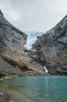 Stunning view of a glacier flowing between rocky cliffs into a turquoise lake.