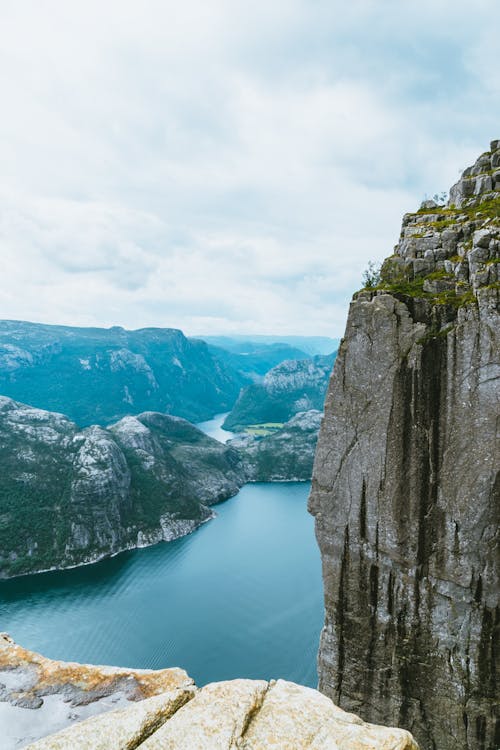 Picturesque scenery of rough rocky mountains covered with moss near wide river with pure rippling water under cloudy sky