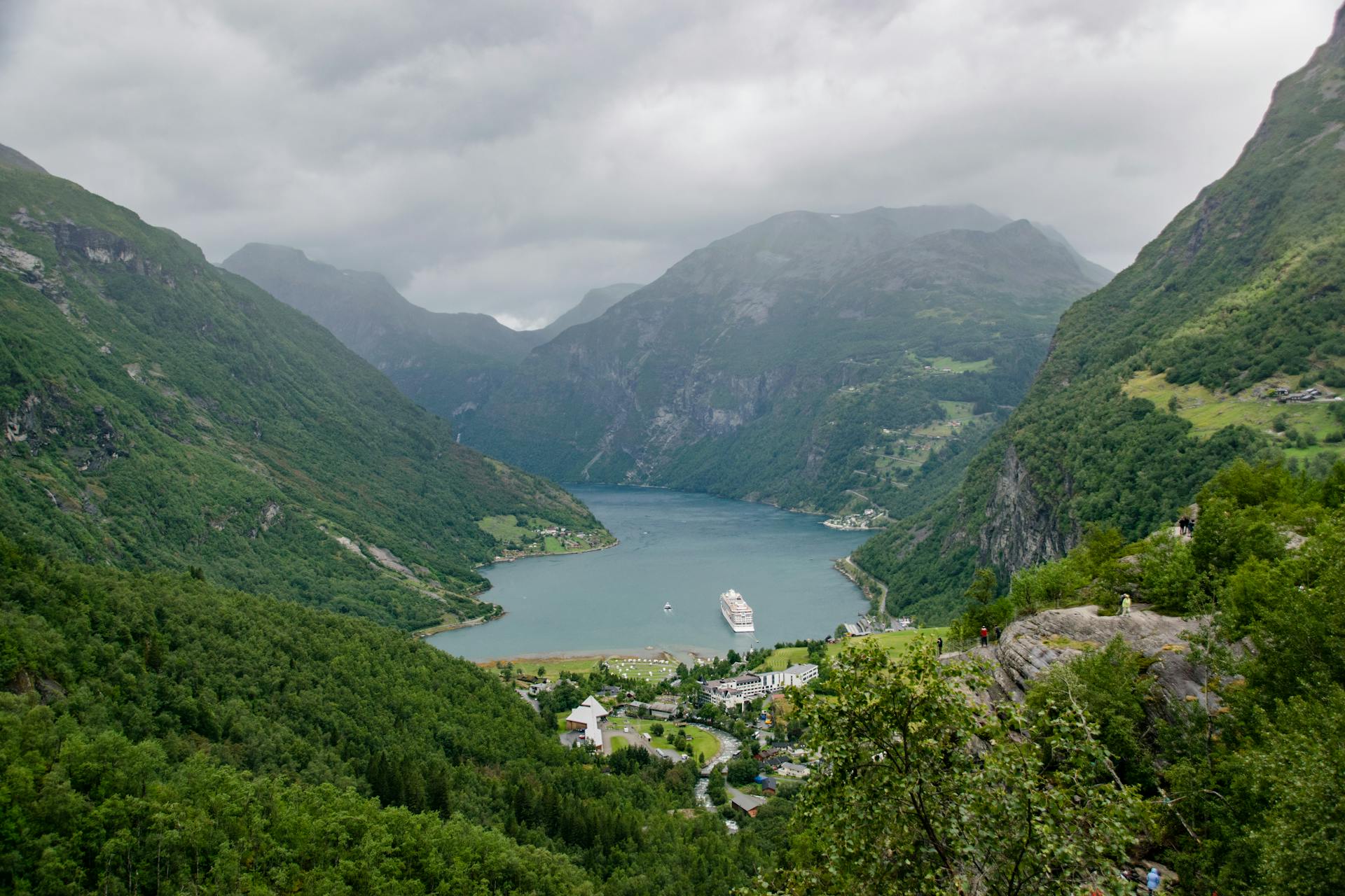 Breathtaking scenery of small village located on shore of mountainous island covered with green trees and plants under overcast sky