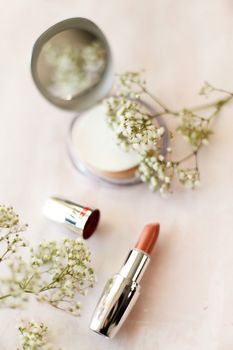 A stunning display of lipstick, compact mirror, and baby's breath in a still life composition.