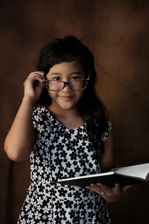 Free Cheerful Asian girl in eyeglasses reading book Stock Photo