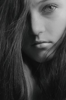 Close-up black and white portrait of a young woman with intense gaze, showing depth and emotion.