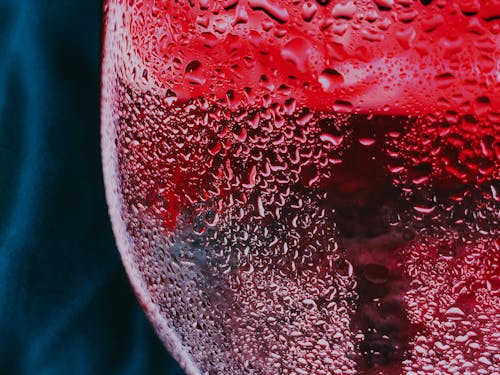 Closeup of water drops on misted glass of cold red fizzy cocktail served on table