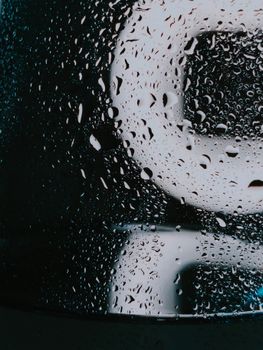 Through wet glass with water drops of white illuminated signboard on rainy night