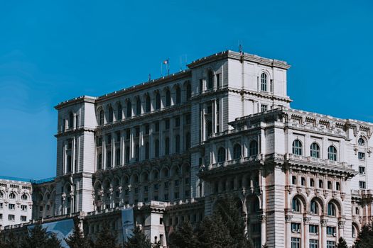 Exterior of aged Palace of the Parliament with arched windows located in Bucharest against cloudless blue sky on sunny day