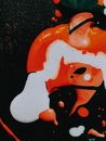 From above of drops and mix of orange and white acrylic paints on black fabric