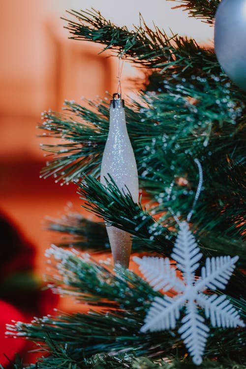 Closeup of decorative icicle and snowflake placed on Christmas tree branch on blurred background at home