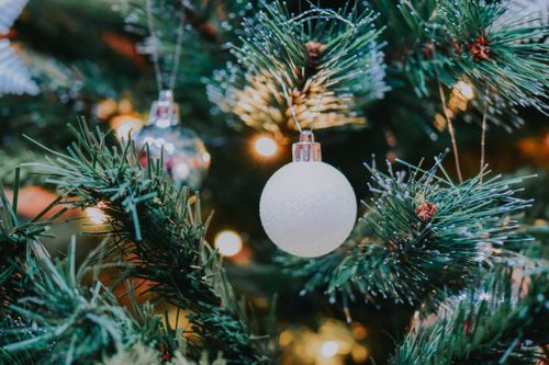 Free Decorative bauble hanging on coniferous tree branch of Christmas tree with glowing garland during festive holiday celebration in light room Stock Photo