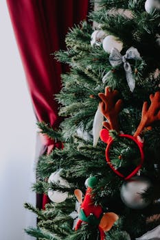 A beautifully decorated Christmas tree indoors adorned with ornaments, ribbons, and an antler headband, capturing the holiday spirit.
