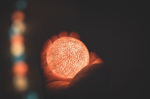 A warm illuminated sphere held by a hand in the dark, showcasing luminescence and contrast.