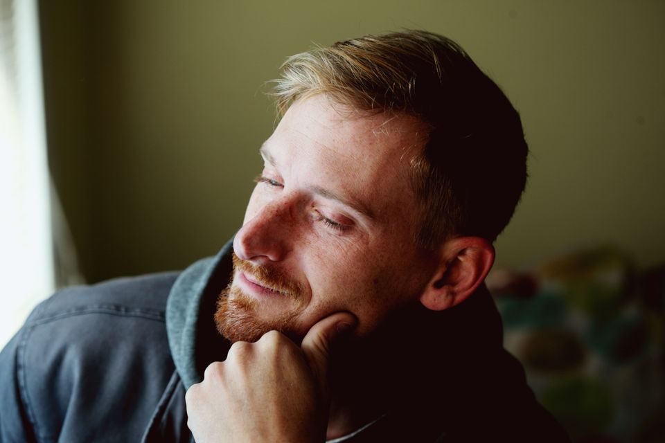 A man with a beard looking thoughtfully out of a window