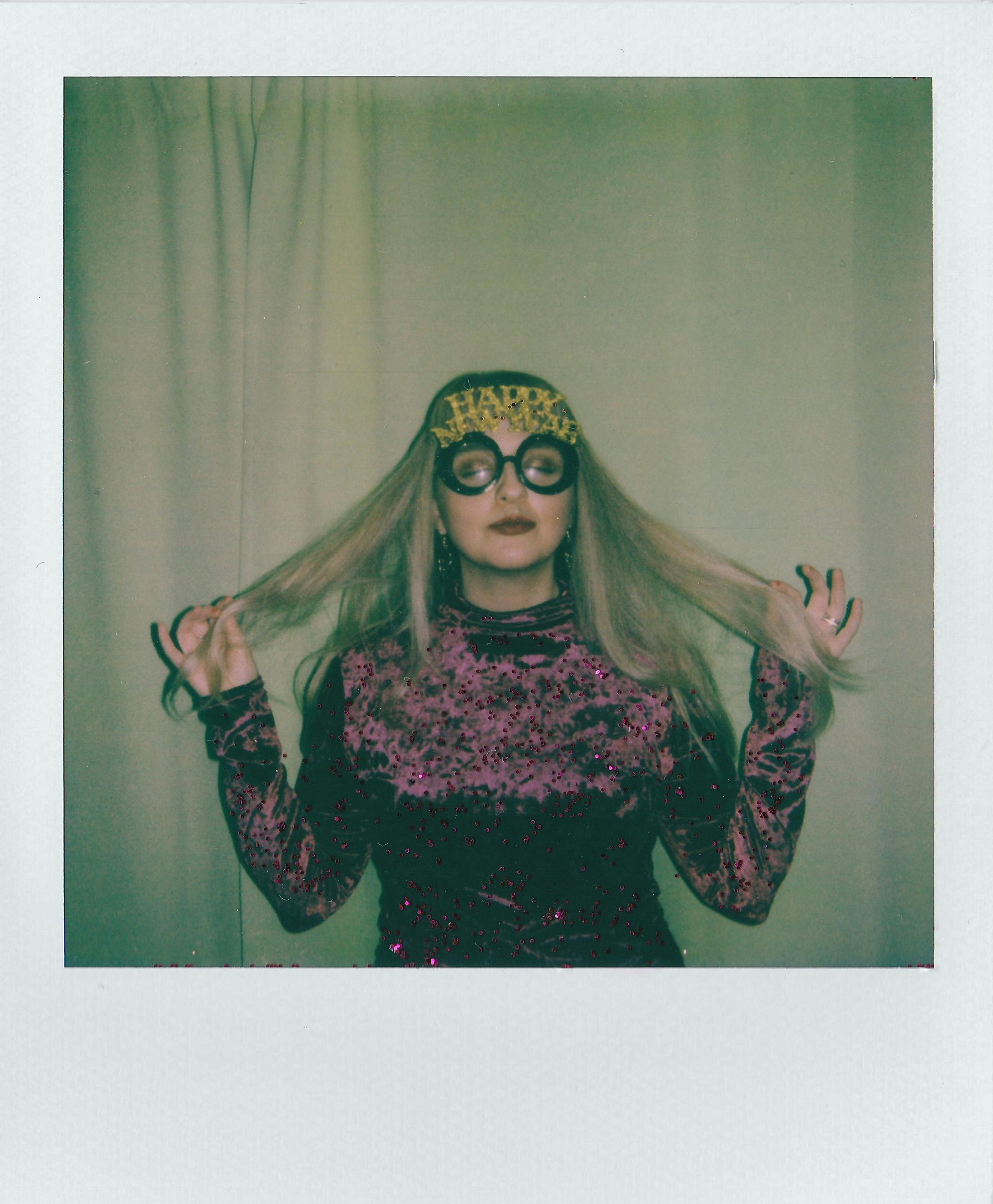 Caucasian woman wearing festive glasses and holding her hair, celebrating New Year's indoors.