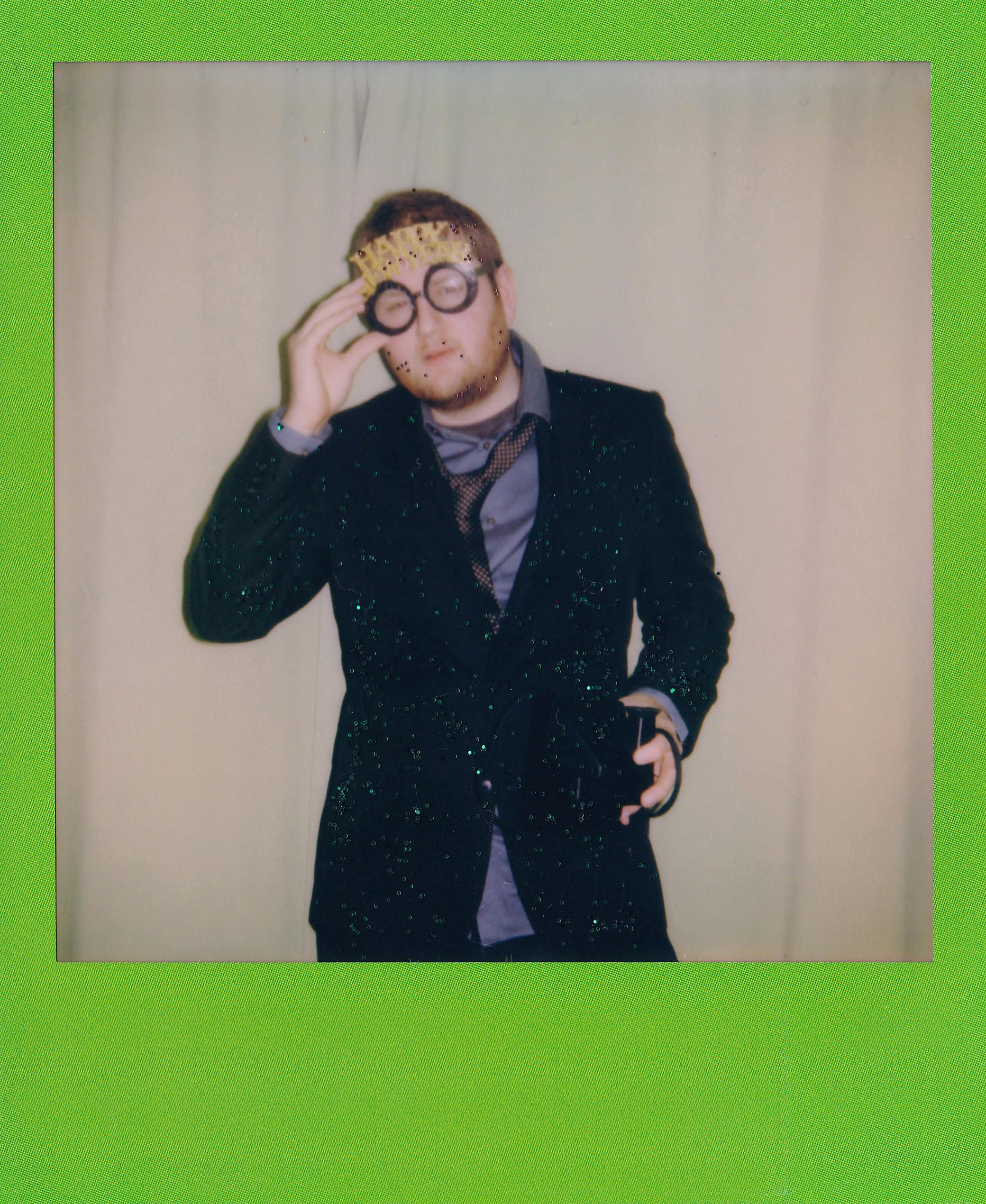 A person in a glittery suit with festive glasses celebrating New Year indoors.