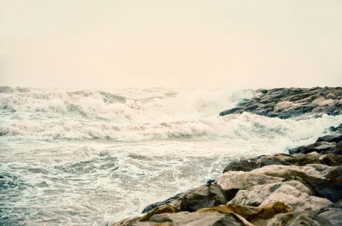 Free Powerful ocean waves crash against rocky coastline under a muted sky, offering a dramatic seascape view. Stock Photo