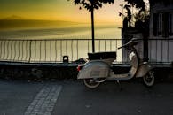 一辆经典的滑板车停在风景优美的栏杆旁，湖面上映照着令人惊叹的日落