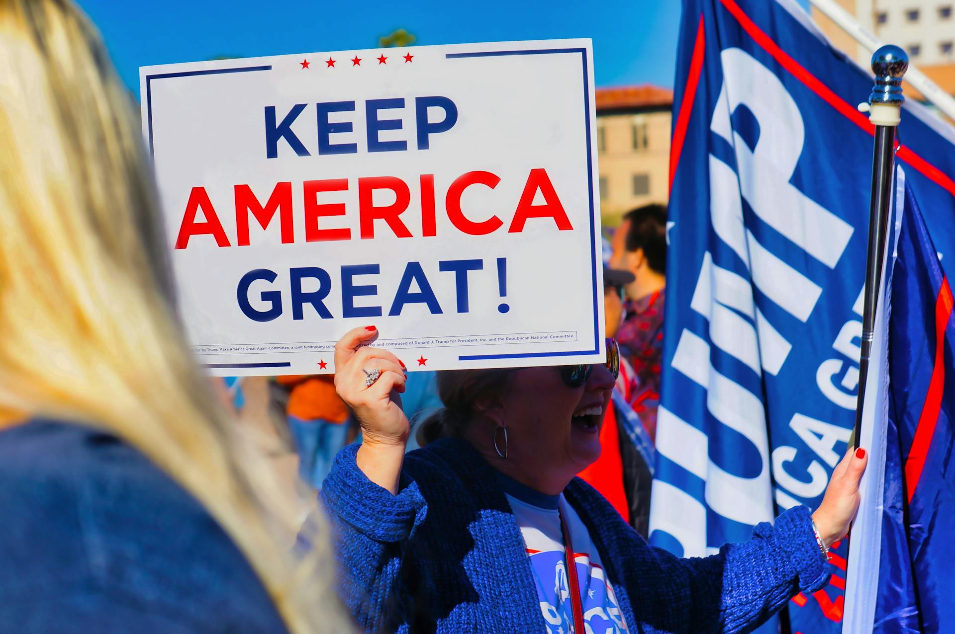 Crowd gathering in Phoenix holding 'Keep America Great' sign at political event outdoors.