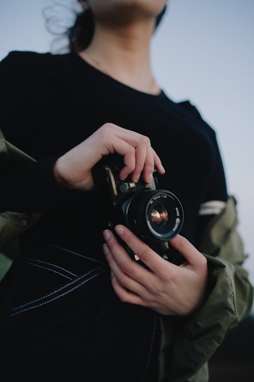Crop unrecognizable woman with photo camera standing in evening nature