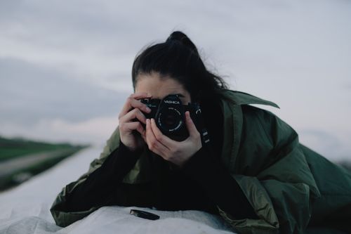 Free Anonymous female photographer in casual wear taking pictures on professional photo camera while lying on roof in countryside in early evening Stock Photo