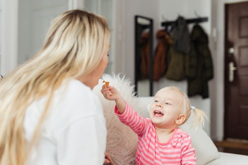Free A heartwarming moment between a mother and her smiling child sharing a snack indoors. Stock Photo