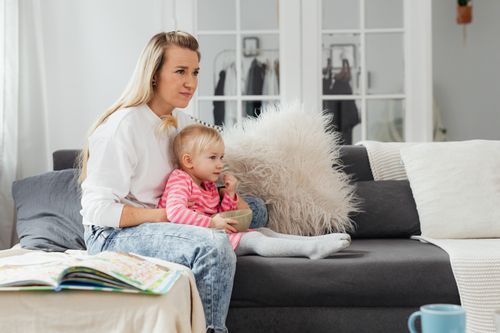 Free A woman and her toddler daughter relaxing on a couch in a cozy living room setting. Stock Photo