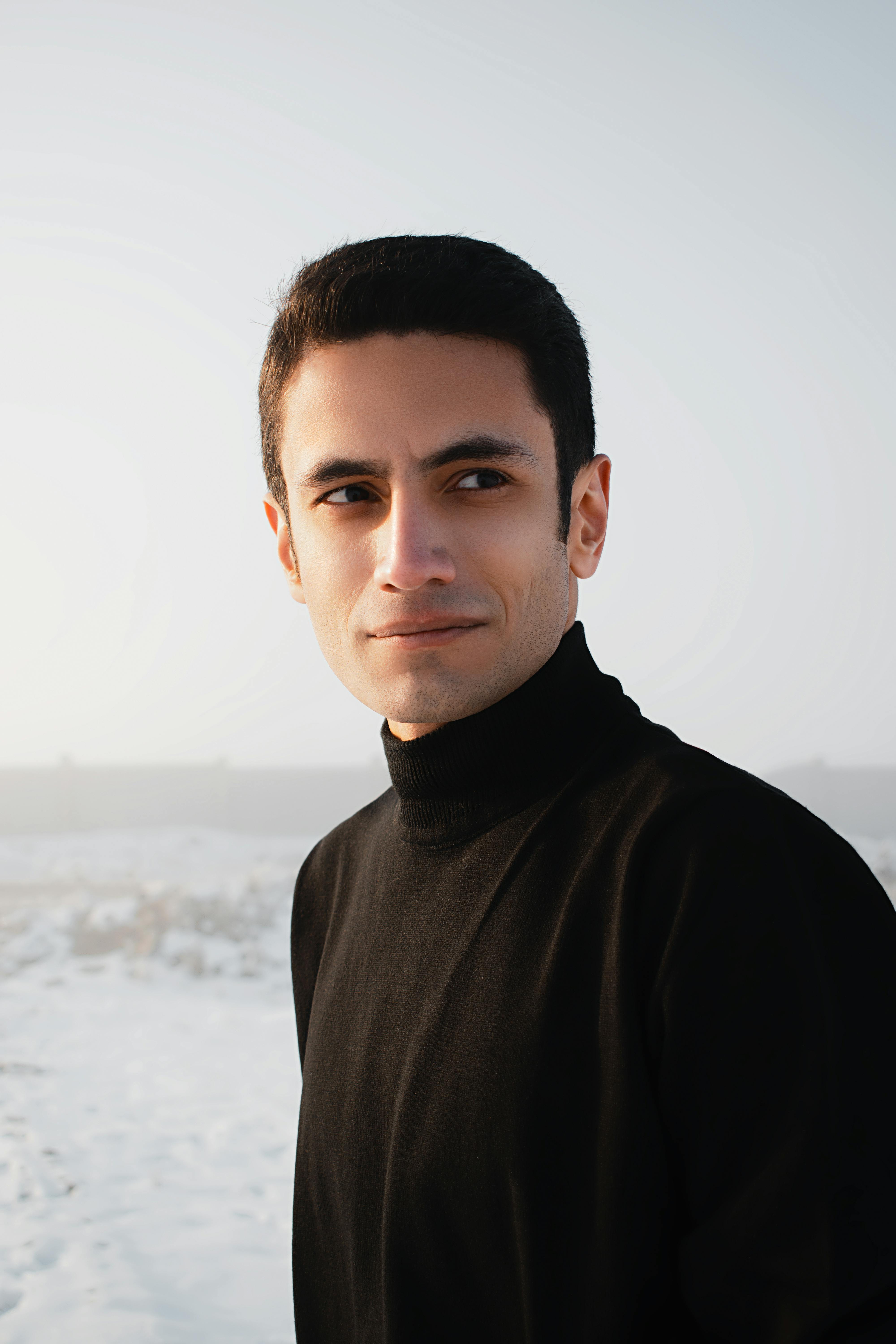 Serious young handsome male in black warm turtleneck in snowy terrain looking away