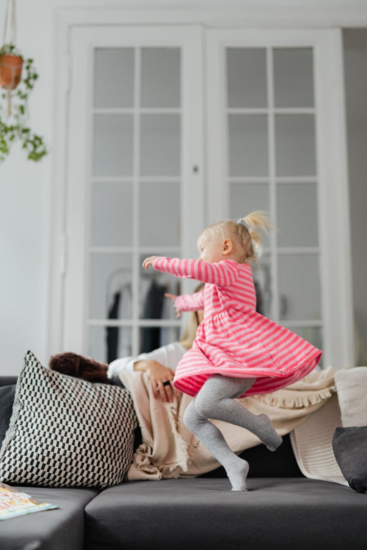 Girl In A Pink Dress Jumping On A Sofa 