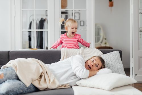 Free A young girl playfully shouting behind a resting mother on a couch in a cozy room. Stock Photo