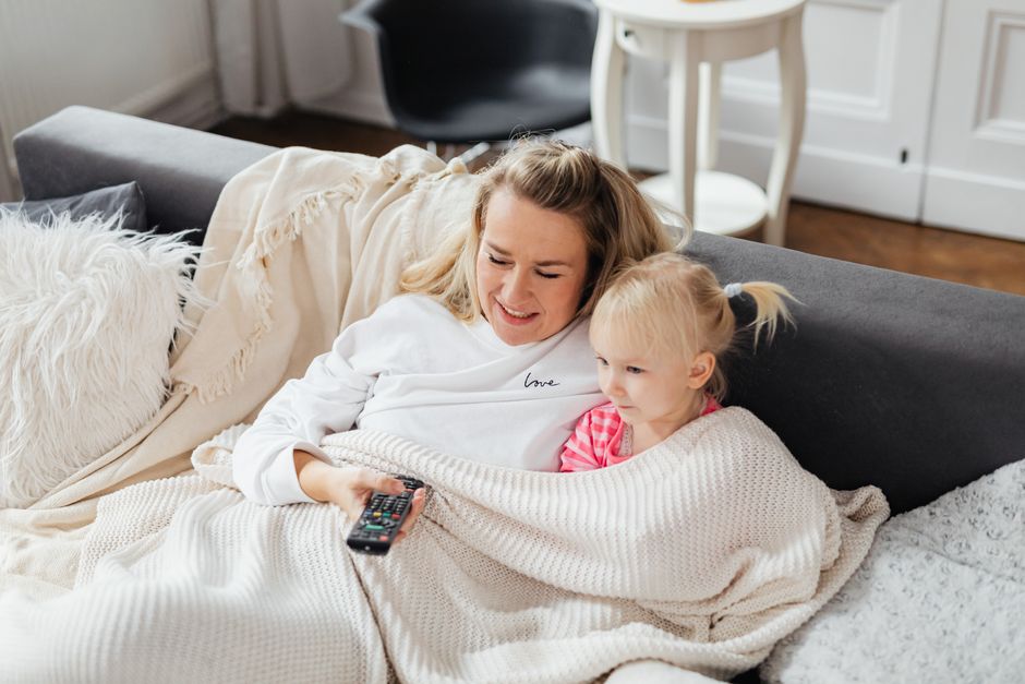A happy single parent relaxing on the sofa while children play in the background - single parent scavenger hunt A happy single parent relaxing on the sofa while children play in the background - single parent scavenger hunt