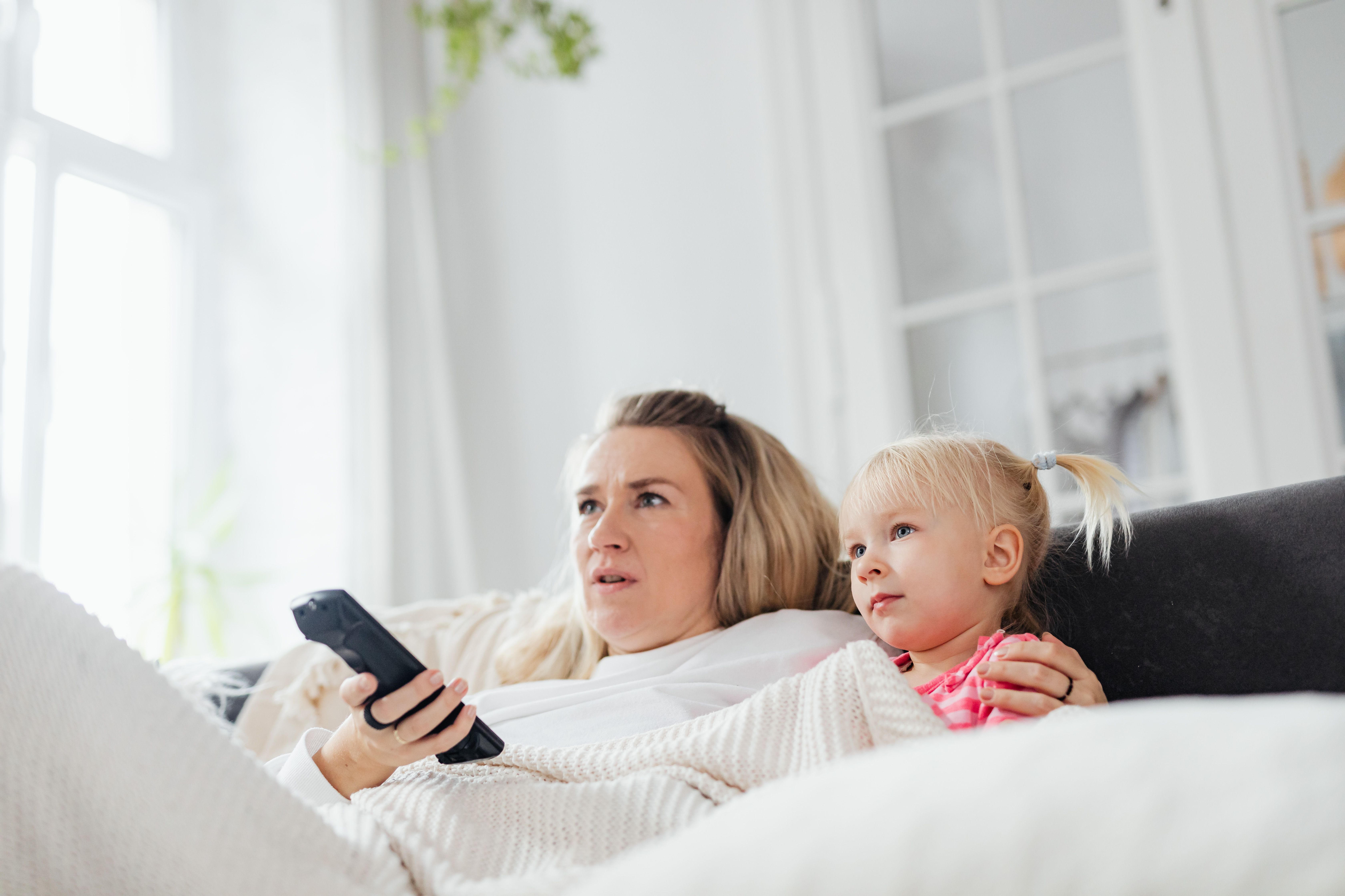 A parent and child in bed holding a TV remote
