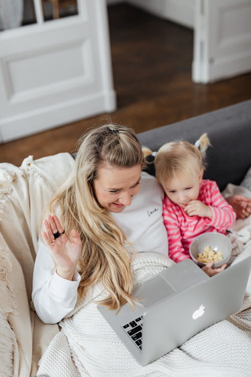 Blonde Girl Eating Popcorn Beside the Woman with a Laptop
