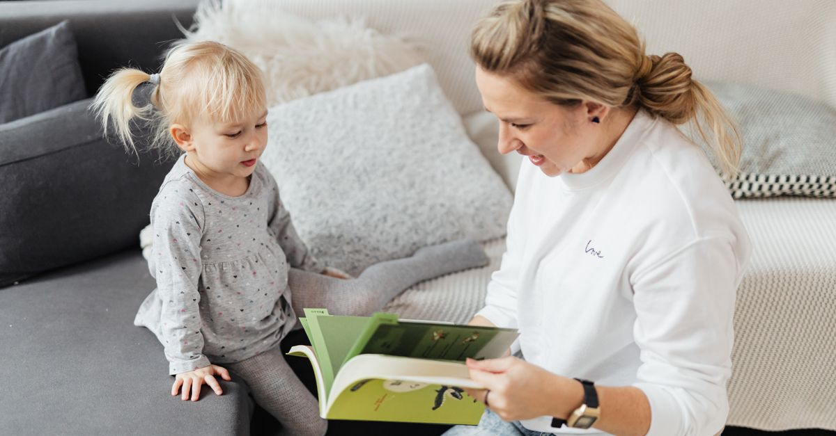 A mother and daughter share a joyful moment reading a book together in a cozy living room setting.