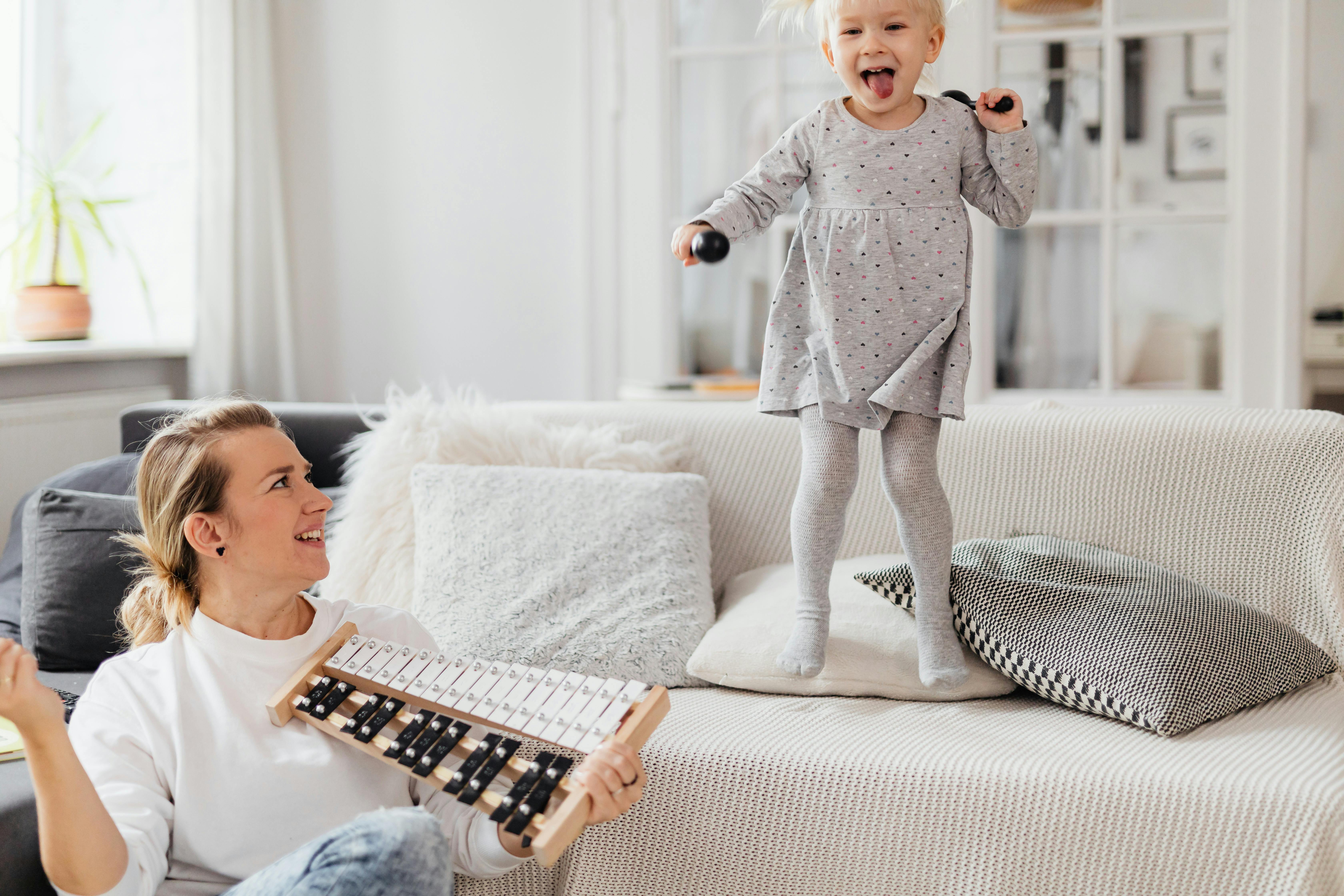 little girl jumping on couch while mother plays on xylophone