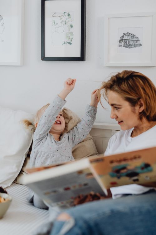 Free A mother reading a book to her joyful daughter in a cozy bedroom setting. Stock Photo