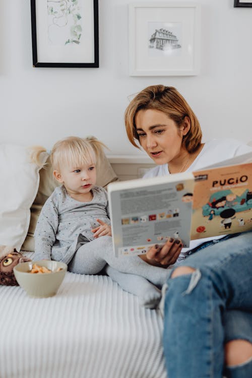 Girl in Blue Denim Jacket Reading Book Beside Girl in Gray Sweater