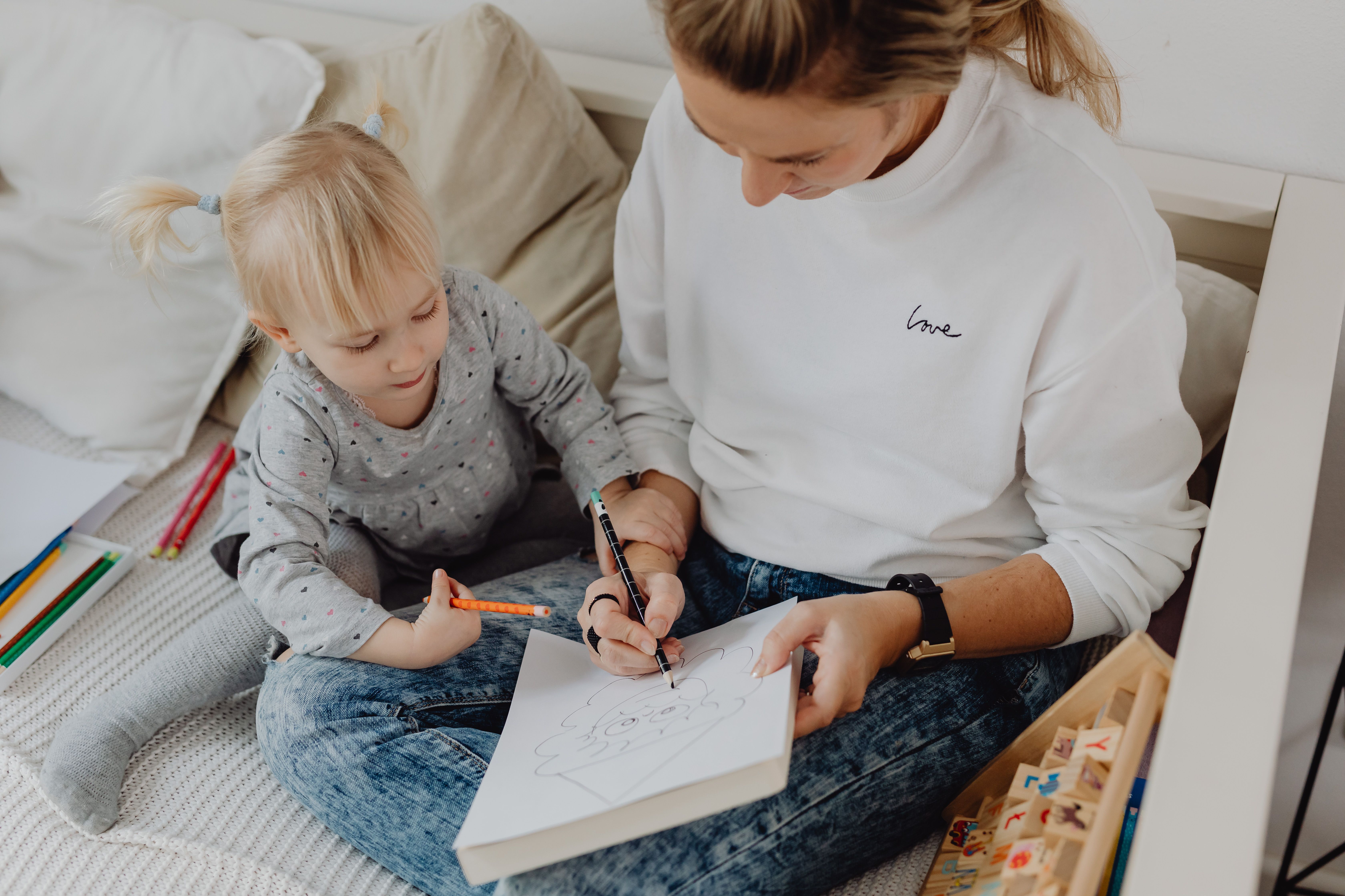 A mother and daughter enjoy drawing together while sitting on a cozy couch.