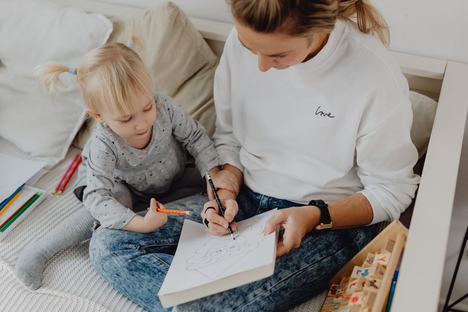 A mother and daughter enjoy drawing together while sitting on a cozy couch.