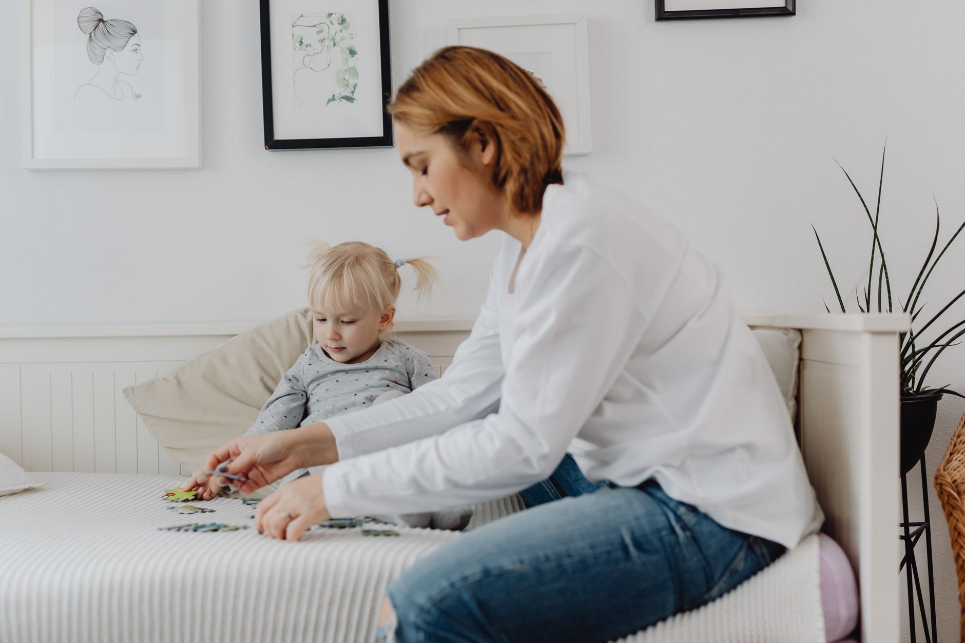 A mother and child enjoy a bonding moment solving puzzles on a bed in a cozy, light-filled bedroom.