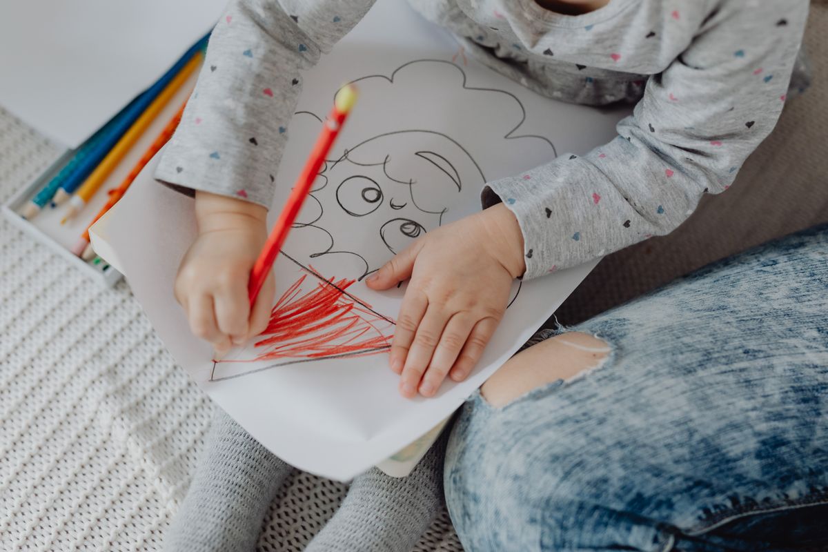 Child drawing with coloured pencils on paper indoors