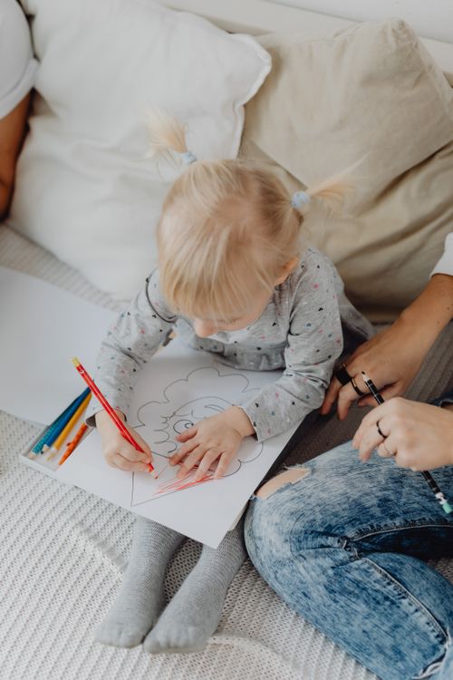 Free Adorable child coloring with colored pencils on a white sofa, focusing intently on her drawing. Stock Photo