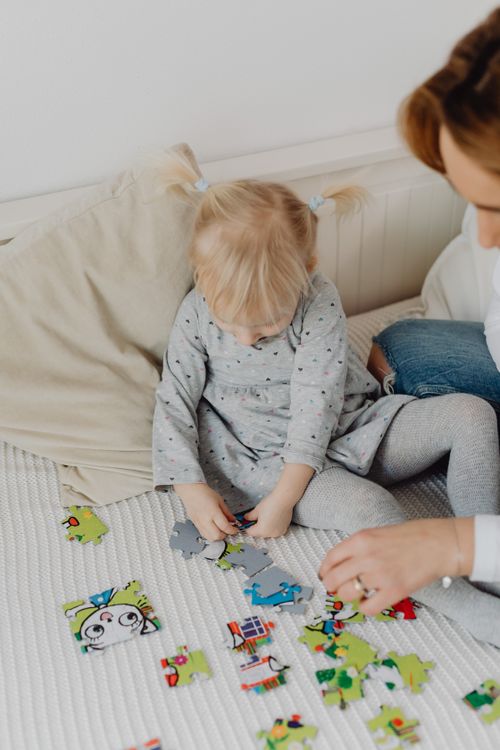 Free A young blonde child solving a colorful puzzle indoors with an adult. Bright and playful scene. Stock Photo
