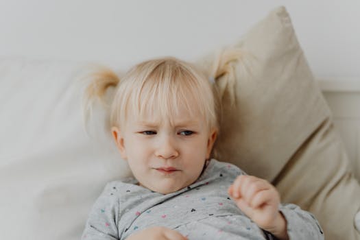 A young blonde child with a displeased facial expression on a light background.
