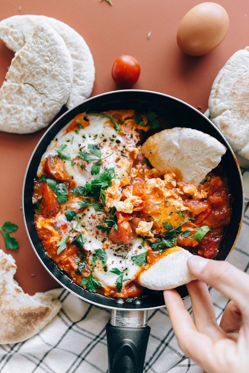 Free Savor a classic Shakshuka dish with vibrant tomatoes, eggs, and herbs served with fresh pita bread. Stock Photo