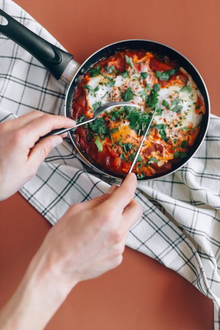 Top view of shakshouka being served with flatware on a tablecloth, showcasing vibrant colors.