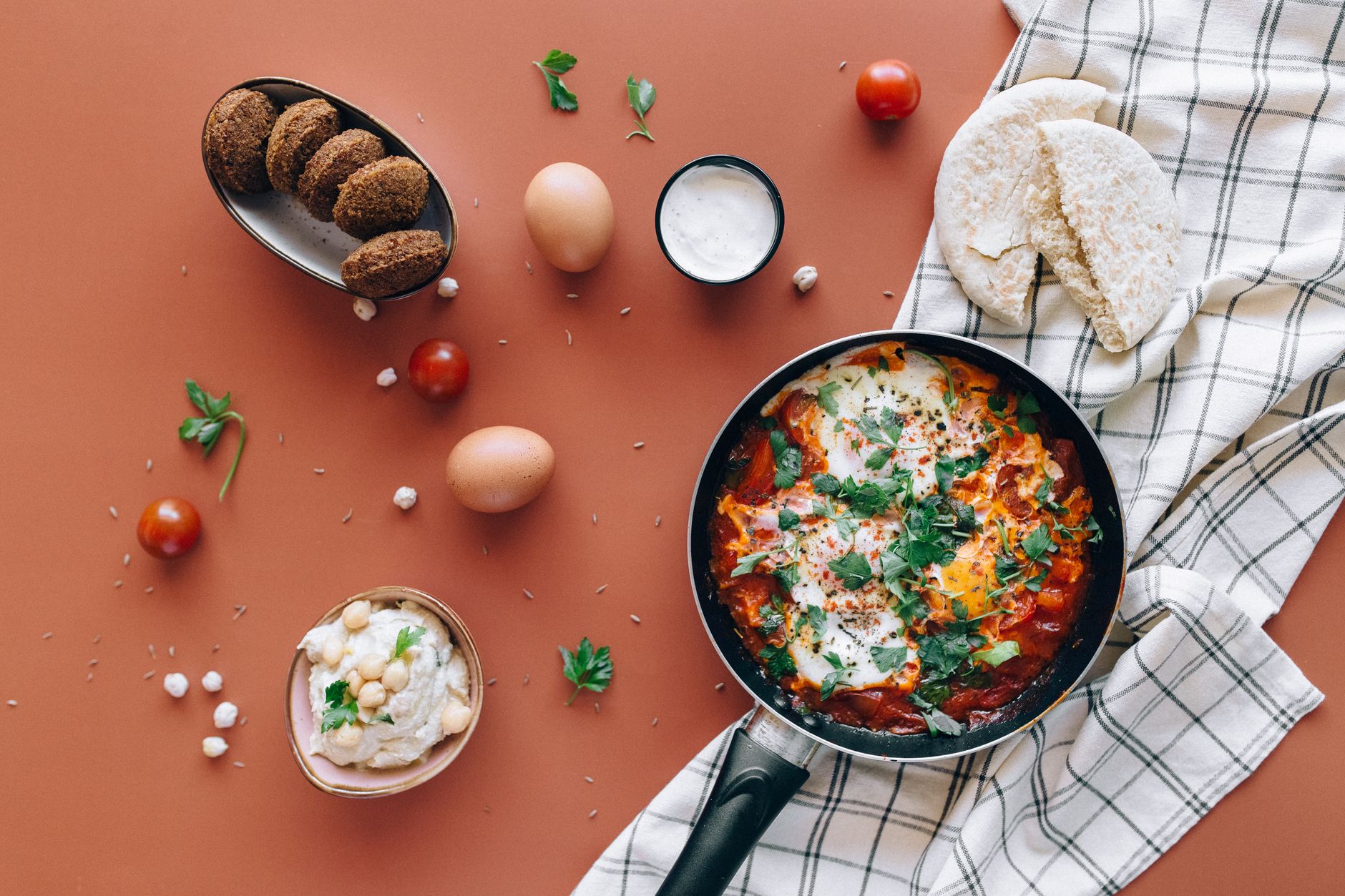 Συνταγή Fitness: Πρωινό Shakshuka 1 Flat lay of Middle Eastern breakfast featuring shakshuka, falafel, pita, and hummus.