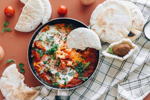 Free Top view of shakshuka meal with pita bread, cherry tomatoes, and fresh herbs. Stock Photo